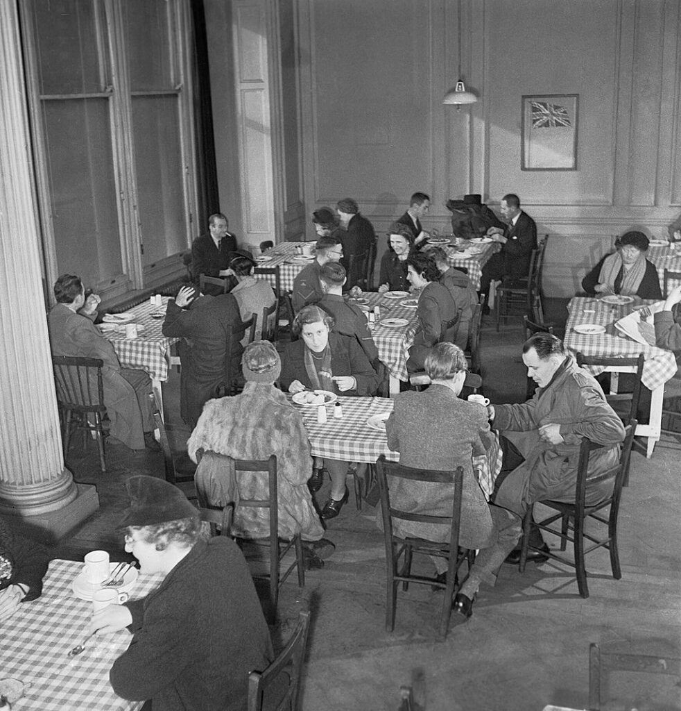 Members of the public seated at communal tables, eating a meal in a British Restaurant in London during the Second World War, 1943. Photograph by Jack Smith for the Ministry of Information