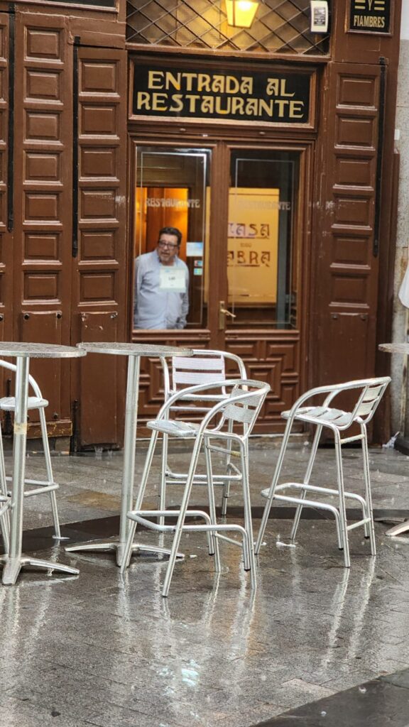 Exterior of Casa Labra in Madrid during a summer rainstorm, with a chef in white uniform looking out from the window.